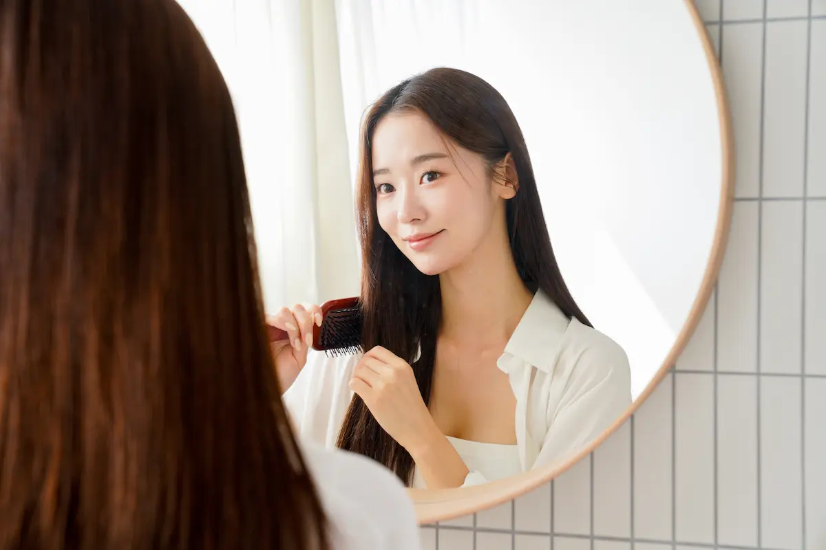 鏡を見ながらブラシで髪をとかす女性