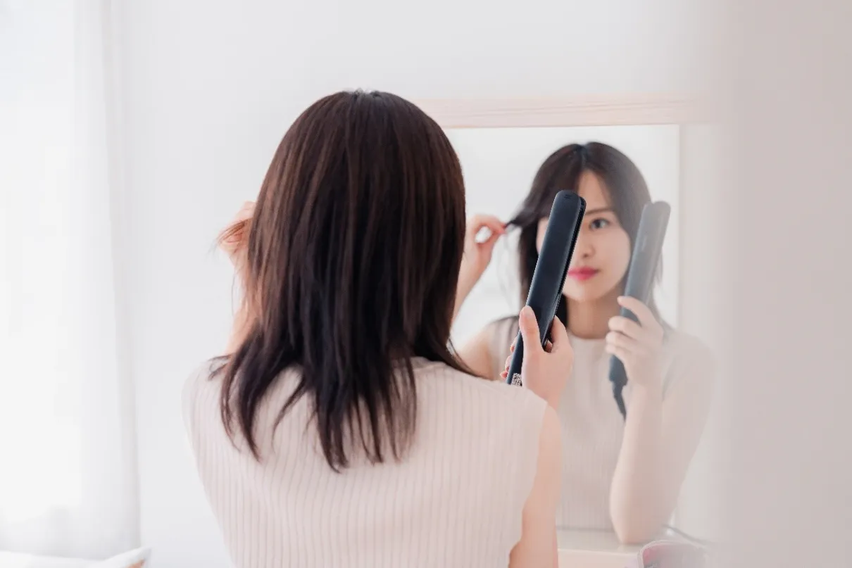 鏡を見ながらヘアアイロンで前髪を整える女性