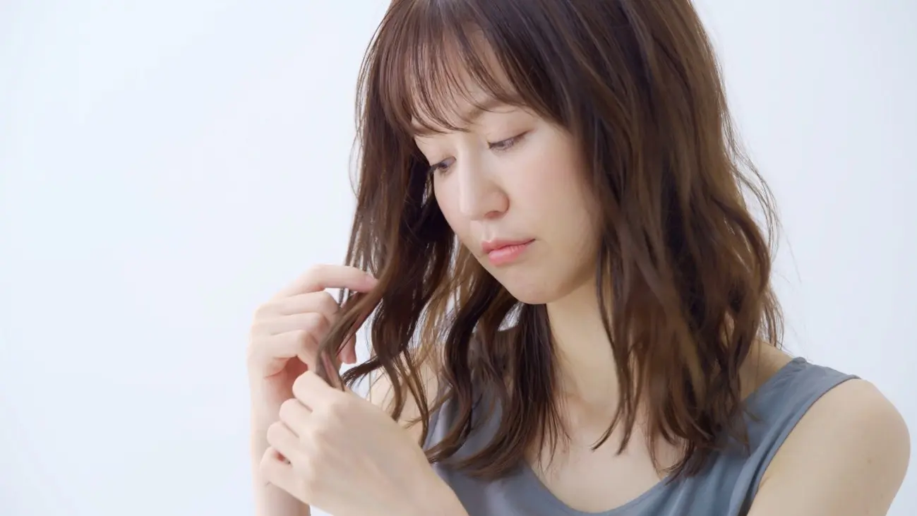 髪の毛を見つめるくせ毛の女性