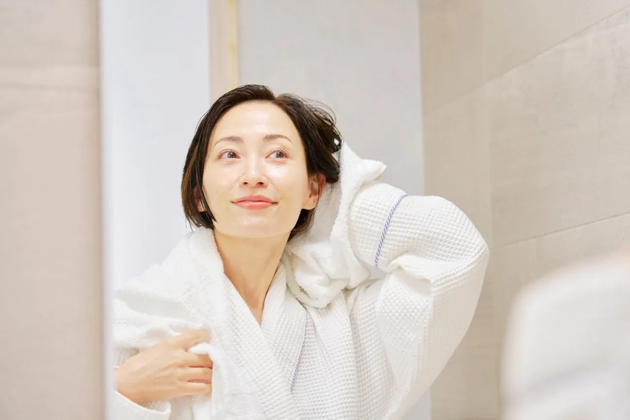 鏡を見ながらタオルで髪を拭くショートカットの女性