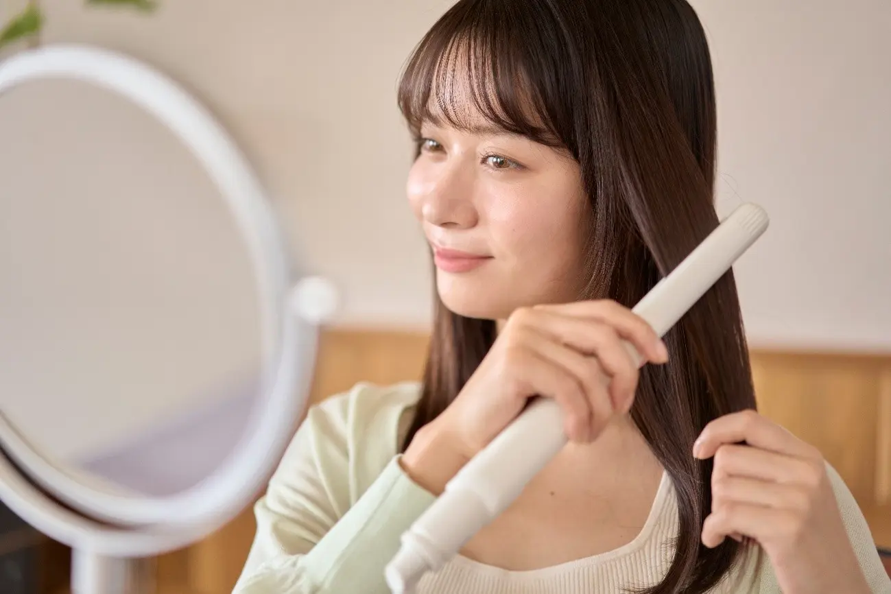 鏡を見ながら髪にストレートアイロンをあてる女性