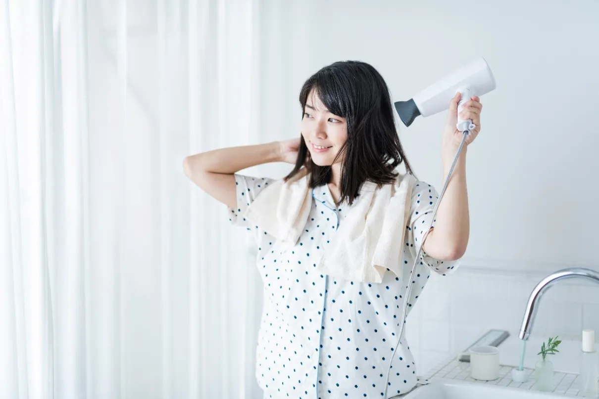 ドライヤーで髪を乾かすパジャマ姿の女性