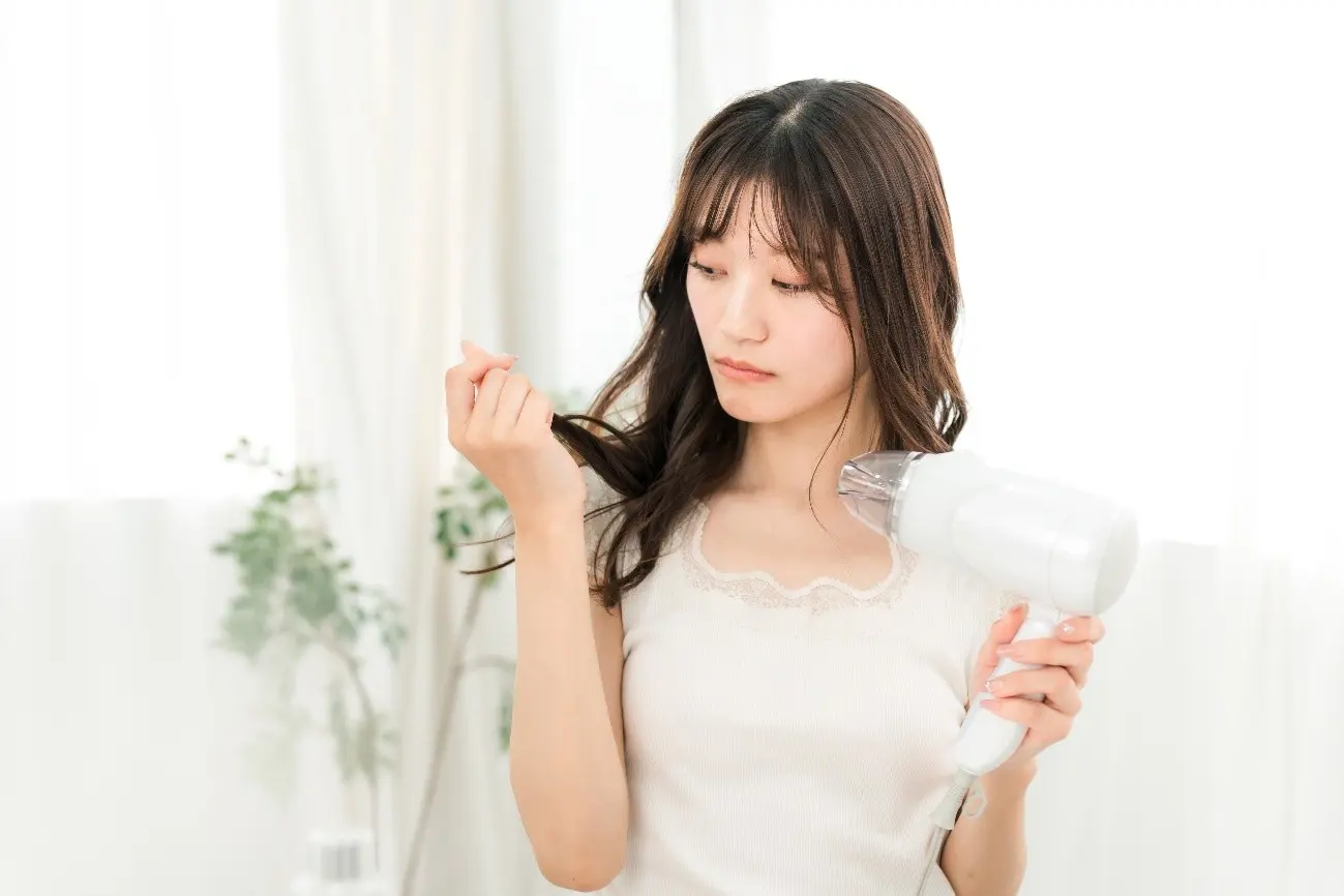 ドライヤーを持ちながら毛先を見るロングヘアの女性