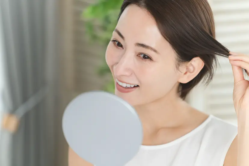 髪を触りながら手鏡を笑顔で見る女性の画像