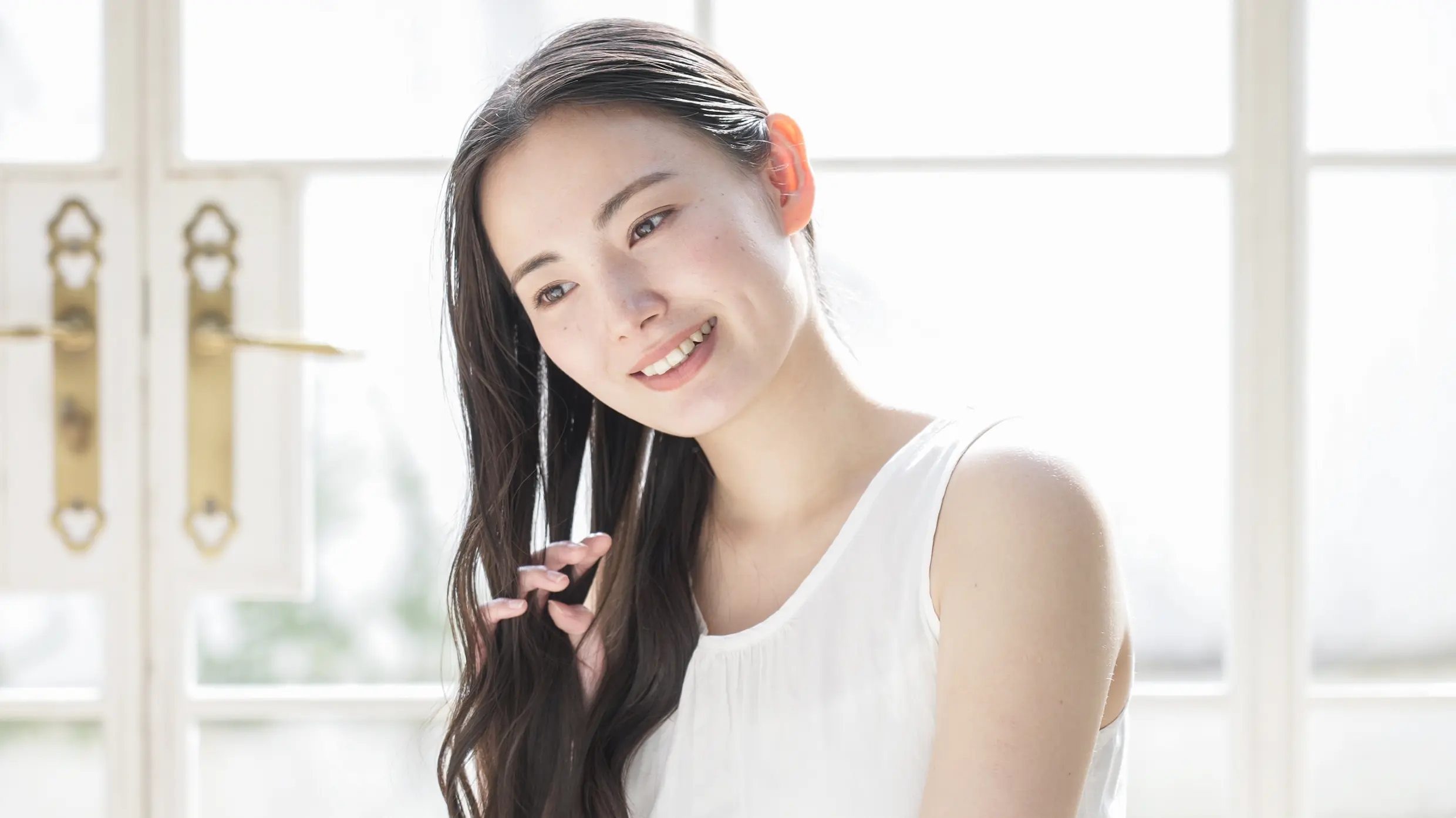 髪の毛を手でとかしながら微笑む女性