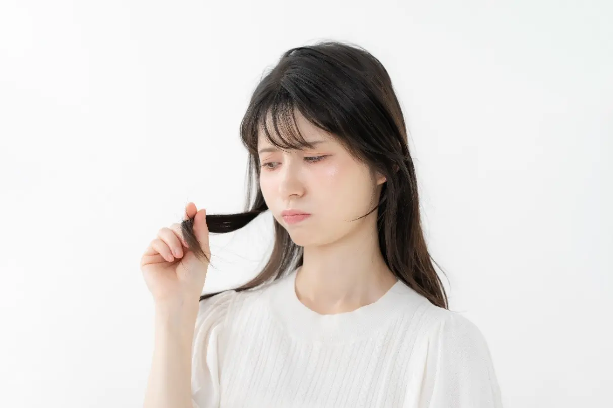 髪の毛先を触りながら不満げな顔をする女性