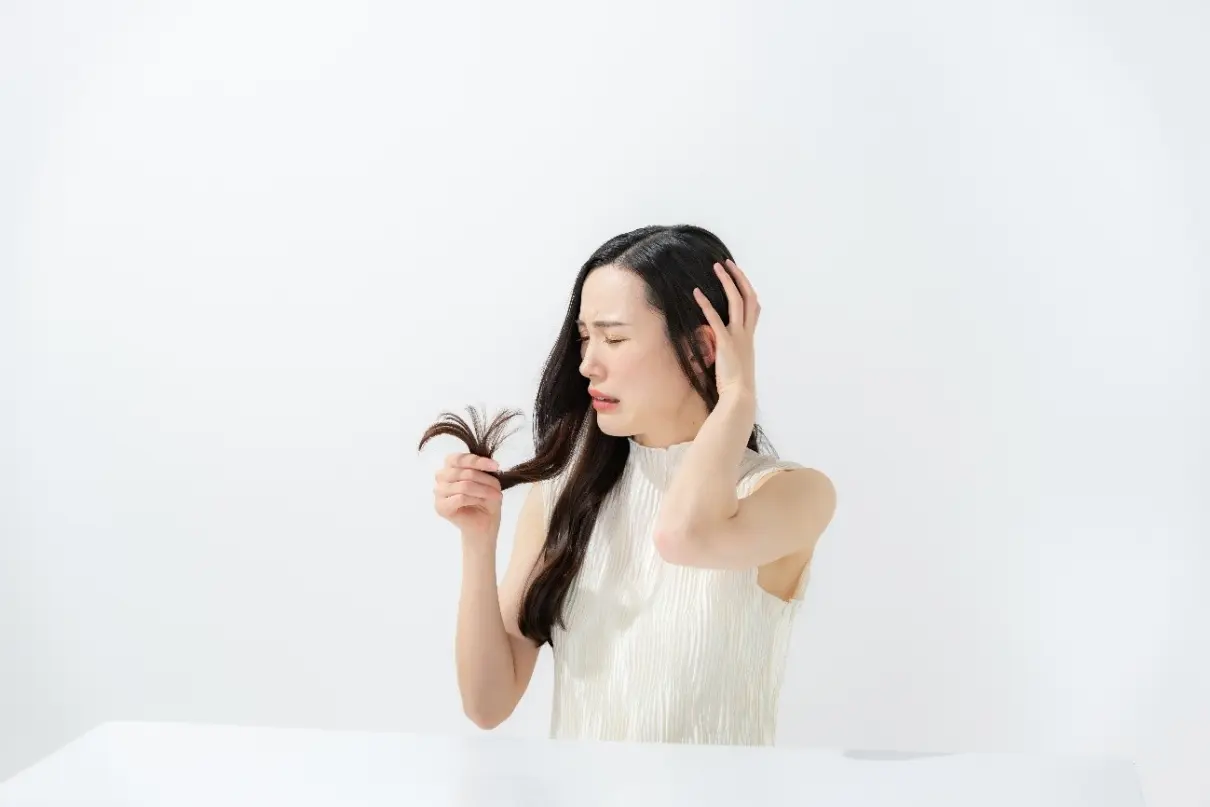 髪の毛先を見つめながら困った顔をする女性